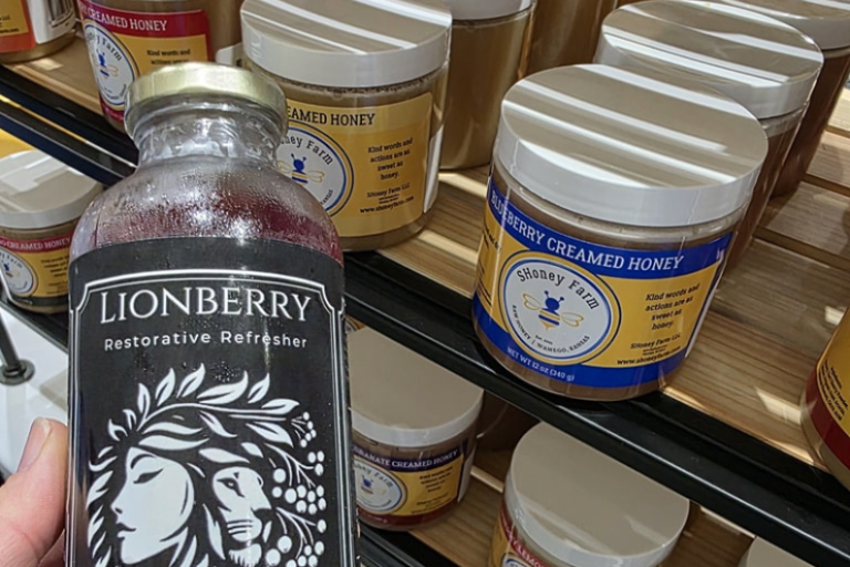 Photo of Lionberry Refresher bottle in front of a display of creamed honey products.